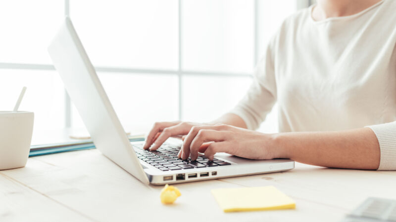 Woman sitting at desk and working at computer hands close up